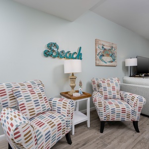 This living area features colorful patterned chairs, a flat-screen TV, and beach-themed decor for a relaxed atmosphere
