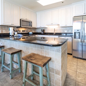 Bright kitchen featuring a granite-topped breakfast bar with rustic stools, modern appliances, and stylish tile backsplash