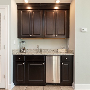 Enjoy preparing drinks at the stylish wet bar with dark cabinetry, blender, ice maker, and granite countertops