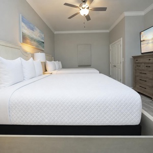 Cozy guest bedroom featuring two queen beds, a large TV, and relaxing coastal vibe