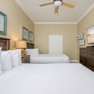 Soothing guest room with two queen beds, coastal artwork, and a large TV for your entertainment