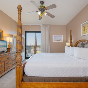 Relax in the spacious master bedroom featuring a four-poster king bed, dresser, and a view through large windows