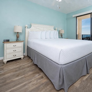 Serene master bedroom features a king bed with soft linens, light blue walls, and a balcony offering a tranquil beach view