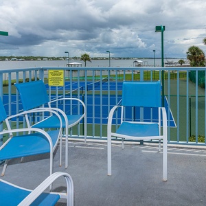 This balcony features blue chairs with a serene lagoon view and nearby tennis courts, perfect for relaxation and leisure