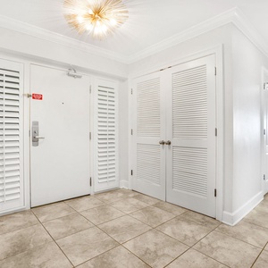 The entryway features elegant tile flooring, white walls, and a stylish light fixture, leading to a bright living area
