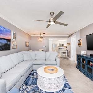 Cozy living area features a large sectional sofa, a TV, and a decorative coffee table, with views leading to the kitchen
