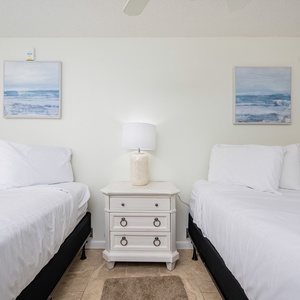 Two queen beds with crisp white linens and coastal artwork create a serene atmosphere in this inviting guest bedroom