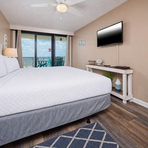 The master bedroom features a comfortable king bed, a wall-mounted TV, and a lovely view from the balcony