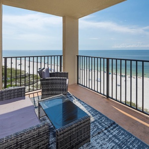 Relax on the balcony with stylish seating, overlooking the beach and vibrant umbrellas dotting the white sand below