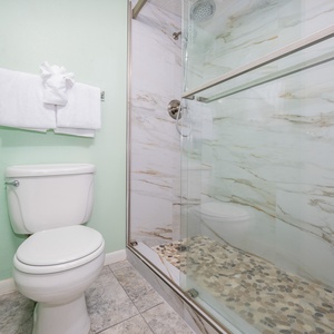 Master bath featuring a walk-in shower with elegant marbled walls and a pebble stone floor, complemented by fresh towels