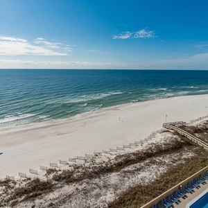 Expansive beachfront view showcasing soft white sand and gentle waves, with a glimpse of the pool area below