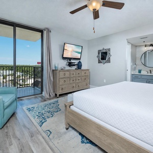 Bright master bedroom featuring a king bed, teal accent chair, dresser, and a balcony with scenic views