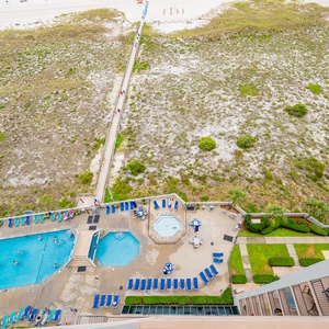 View of the pool area featuring a large swimming pool, kiddie pool, and lounge chairs, with a pathway leading to the beach