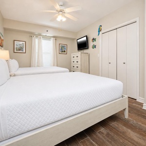 Bright and airy guest bedroom featuring two queen beds, a wall-mounted TV, and cheerful coastal decor for a relaxing stay