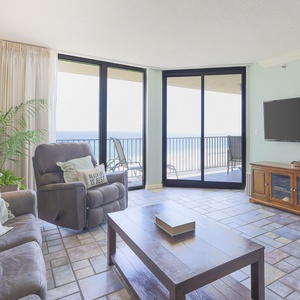 Cozy living area features a plush sofa, recliner, and a view of the beach through large sliding glass doors