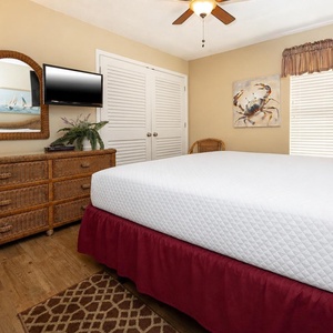 This cozy guest bedroom features a charming wicker dresser, a mounted TV, and nautical decor