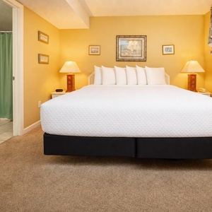 The master bedroom features a plush king bed with multiple pillows, warm yellow walls, and en-suite bathroom