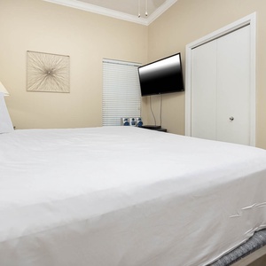 A cozy bedroom features a plush king bed with white linens, a mounted TV, and soft lighting for a restful atmosphere