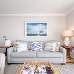 Cozy living room featuring a light gray sofa adorned with colorful pillows, a woven coffee table, and nautical artwork