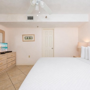 White linens invite deep rest in the king suite beneath a fan and floral artwork on soft walls