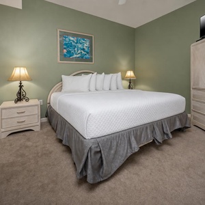 This cozy bedroom features a plush king bed, soft carpeting, and warm lighting from bedside lamps against a green wall