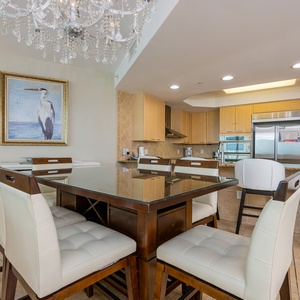 Elegant dining area featuring a glass-top table, plush white chairs, and a stunning chandelier in a modern kitchen setting