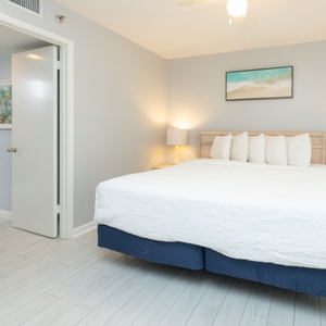 Guest bedroom featuring a large king bed with white linens, a TV on a stylish shelf, and a colorful coastal artwork above