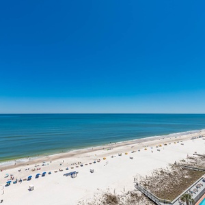 Expansive beachfront view showcasing white sand, colorful umbrellas, and a serene blue sea under a clear sunny sky