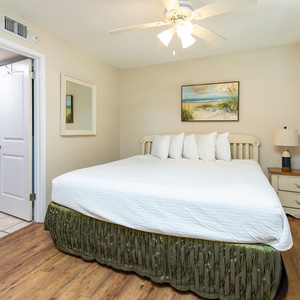 Brightly lit guest bedroom featuring a large king bed with crisp white linens, a bedside lamp, and a beach painting above