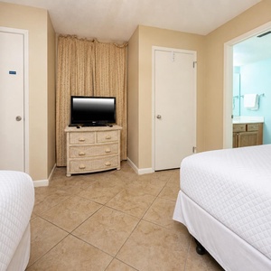 Guest room featuring two comfortable double beds, a TV, and a doorway leading to a light blue bathroom