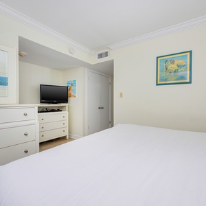 The bedroom features a comfortable bed, a TV for entertainment, and cheerful artwork, perfect for relaxation