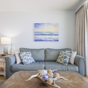 This living area features a comfortable blue sofa, decorative pillows, a stylish coffee table, and a beautiful beach view