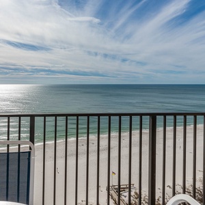 A serene view of the beach stretches below, framed by a balcony railing and showcasing the calm, glistening waters