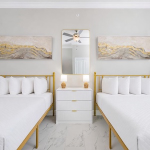 Stylish guest bedroom featuring two queen gold bed frames, decorative artwork, and a relaxing vibe