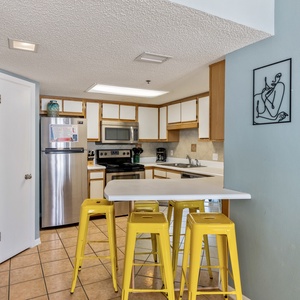 Bright kitchen features a breakfast bar with yellow stools, stainless appliances, and artistic wall decor for a cheerful vibe