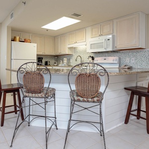 Charming breakfast bar with woven seating complements the kitchen featuring light cabinetry and decorative tile backsplash