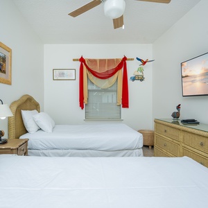 Cozy guest bedroom features two twin beds, a flat-screen TV, and tropical decor for a cheerful stay