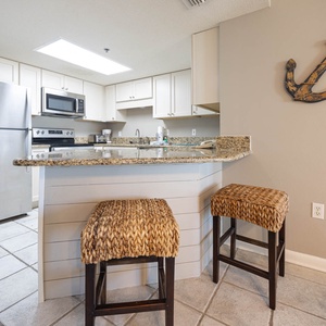 Modern kitchen area features a breakfast bar with woven stools, granite countertops, and a nautical-themed wall accent