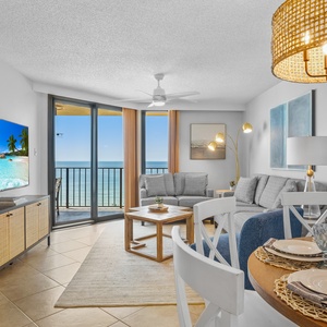 Bright living area featuring a cozy sofa, dining table set for four, and expansive glass doors revealing a beach front view
