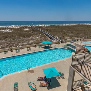 Expansive pool area with turquoise umbrellas and sun loungers, leading to the beach and inviting views of the gulf