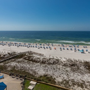 The view showcases a pristine beach with white sand and colorful umbrellas, inviting relaxation under a clear blue sky