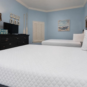 This guest bedroom features two comfortable queen beds, a TV, and beach-themed decor against soft blue walls