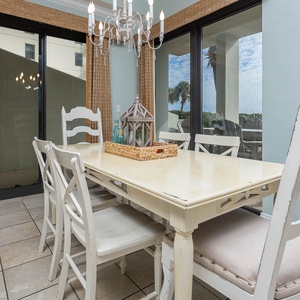 Dining area features a wooden table with white chairs, accented by a decorative centerpiece and views of the pool outside