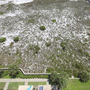 Lush greenery and white sand stretch across the landscape, leading to a serene beach access path framed by palm trees