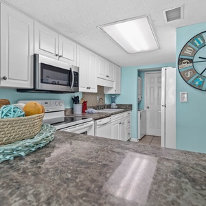 Bright kitchen featuring white and stainless appliances, granite countertops, and decorative coastal accents
