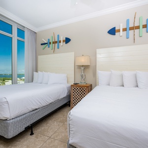 Rest comfortably in this guest bedroom featuring two queen beds, coastal decor, and large windows with scenic views
