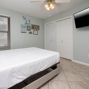This guest bedroom features a comfortable queen bed, wall-mounted TV, and beach-themed decor for a relaxing stay