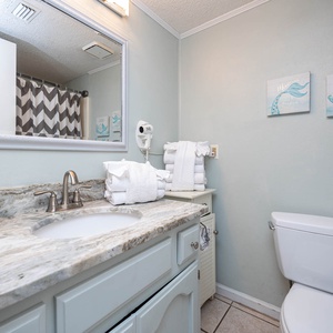 The guest bath features a stylish granite countertop, plush towels, and a relaxing shower curtain with a chevron pattern