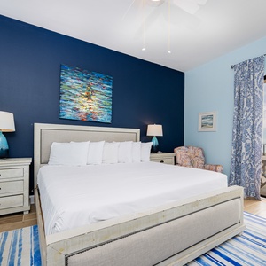 Brightly decorated bedroom features a king bed, colorful art, and a cozy chair, with access to a beach view balcony