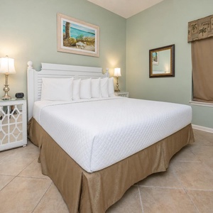 Brightly decorated bedroom featuring a king bed, bedside lamps, a TV, and tropical artwork enhancing the relaxing atmosphere